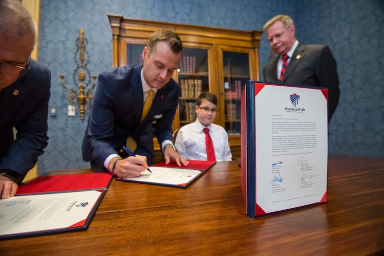 Andrew Newby (left center), assistant director for Veteran and Military Services, signs a proclamation declaring Ole Miss Wish Kid Benjamin Clark as ‘Kid President’ of the University of Mississippi on Friday (Nov. 2) as Chancellor Jeffrey Vitter looks on at the Lyceum. The proclamation states that all future Ole Miss Wish recipients will also serve as ‘Kid President.’ Photo by Kevin Bain
