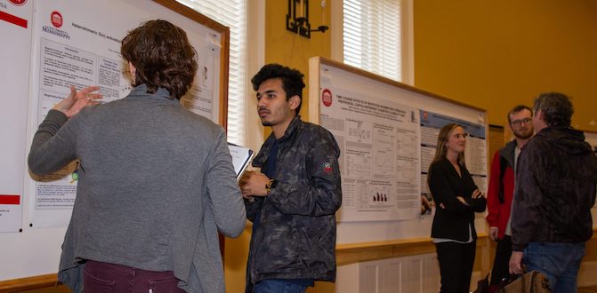Participants in the UM Neuroscience Research Showcase poster competition examine and discuss their presentations. 